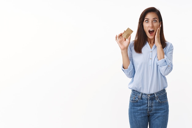 Astonished middle-aged woman impressed how fast received new credit card, touch cheek drop jaw surprised, amazed big reasonable cashback satisfied online banking system, stand white wall