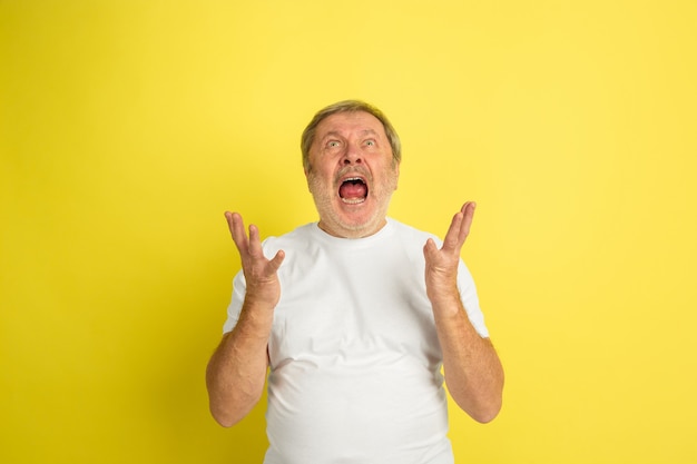 Astonished, shocked, wondered screams. Caucasian man portrait isolated on yellow studio background. Beautiful male model in white shirt posing. Concept of human emotions, facial expression, sales, ad.