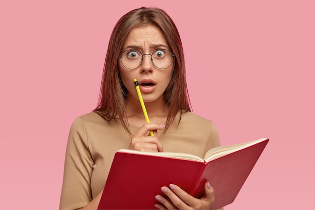 Astonished student keeps red organizer and pencil