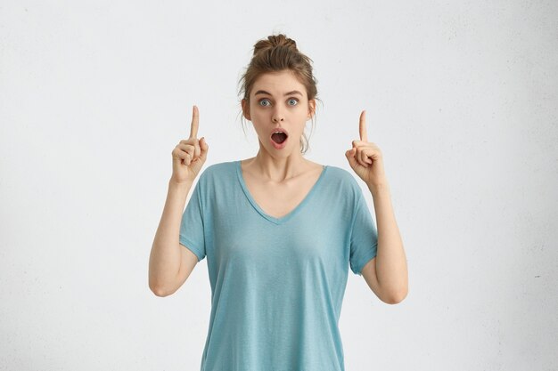 Astonished teenage girl indicating something surprising and shocking on white studio wall