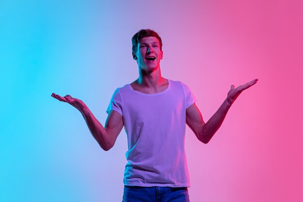 Astonished. Young caucasian man's portrait on gradient blue-pink studio background in neon light. Concept of youth, human emotions, facial expression, sales, ad. Beautiful model in casual.