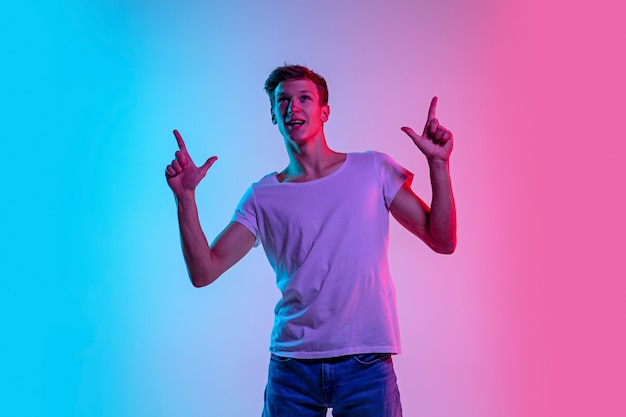 Astonished. Young caucasian man's portrait on gradient blue-pink studio background in neon light. Concept of youth, human emotions, facial expression, sales, ad. Beautiful model in casual.