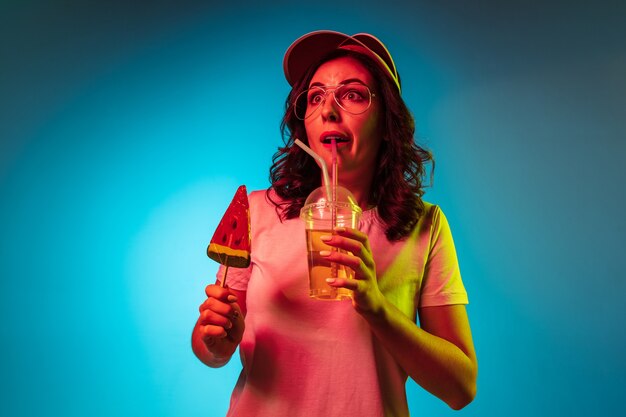 유행 블루 네온 스튜디오를 통해 과자와 음료를 들고 모자에 놀란 젊은 여자
