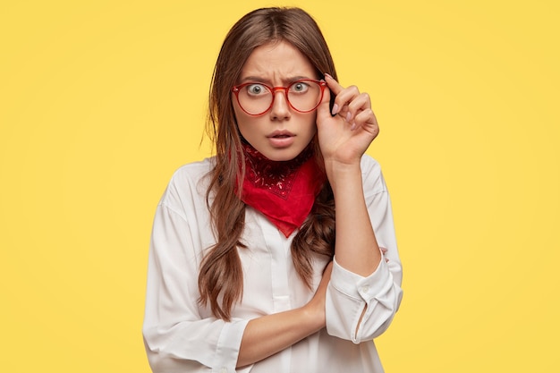 Free photo astounded young brunette with glasses posing against the yellow wall