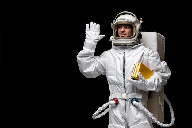 白い宇宙服の宇宙飛行士の日の宇宙飛行士は、ハイサインを振って本の山を保持しているガラスのヘルメットを開きます