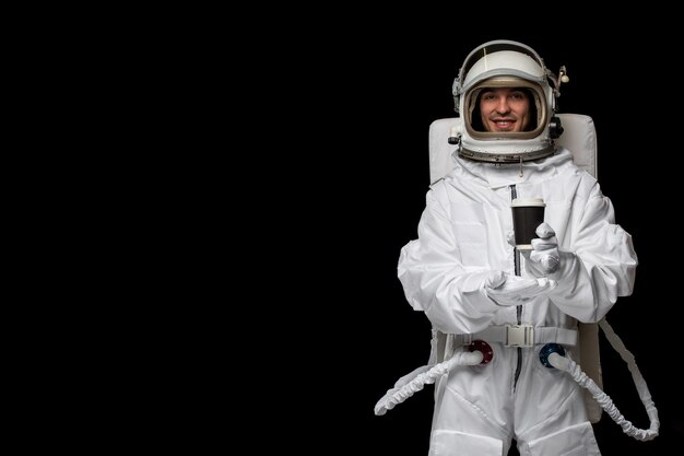 흰색 우주복을 입은 우주인의 날 우주인은 검은 컵을 들고 열린 유리 헬멧을 웃고 있습니다.
