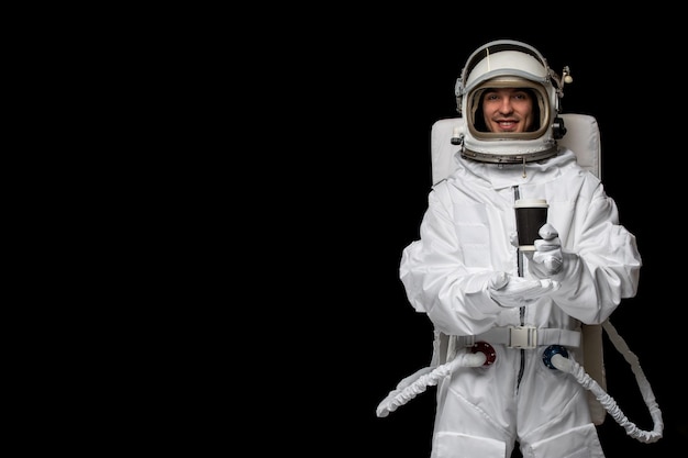 黒いカップを保持している開いたガラスのヘルメットを笑顔の白い宇宙服の宇宙飛行士の日の宇宙飛行士