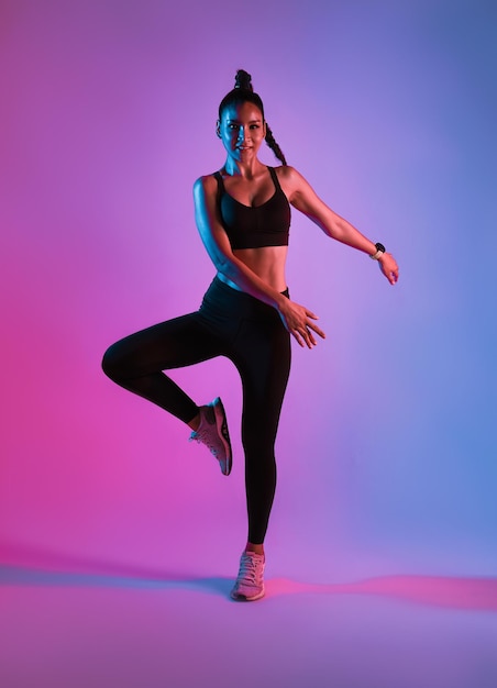 Спортсменка азиатская спортсменка прыгает в танце в рамках тренировки по сжиганию жира на фитнес-неоновом фоне