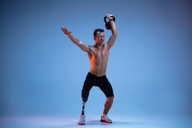 Спортсмен с ограниченными возможностями или инвалидом, изолированные на синем фоне студии. Профессиональный спортсмен-мужчина с тренировкой протезирования ноги с гирями в неоне.