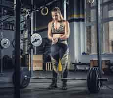 Free photo athletic blond female fitness model holding heavy barbell and preparing for squats.