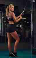 Free photo athletic blonde woman in sportswear posing while doing exercise on the triceps on the crossover machine in the gym.