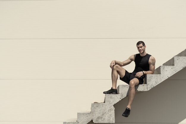 Athletic carefree sportsman posing while sitting and smiling on stairs