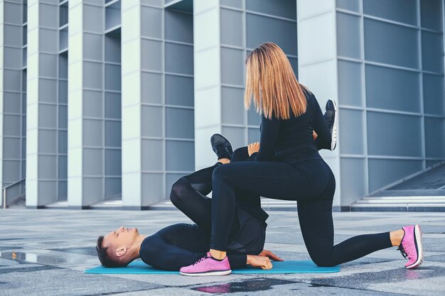 The athletic fitness couple is exercising on an aerobic mat over modern building background.