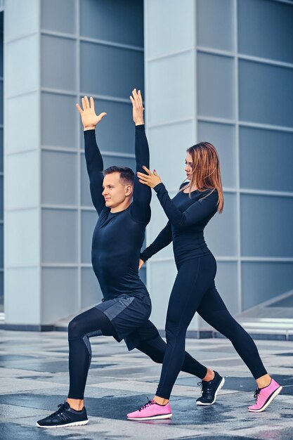 The athletic fitness couple is stretching over modern building background. Full body image.