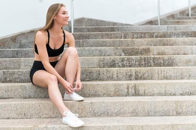Спортивная девушка стоит на лестнице и завязывает шнурки