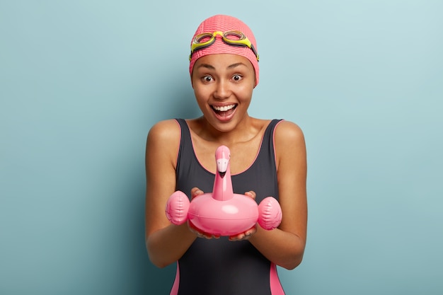 무료 사진 수영 의상을 입은 운동 기쁜 여자, 고글 착용, 플라밍고 모양의 분홍색 팽창 수영 반지 보유