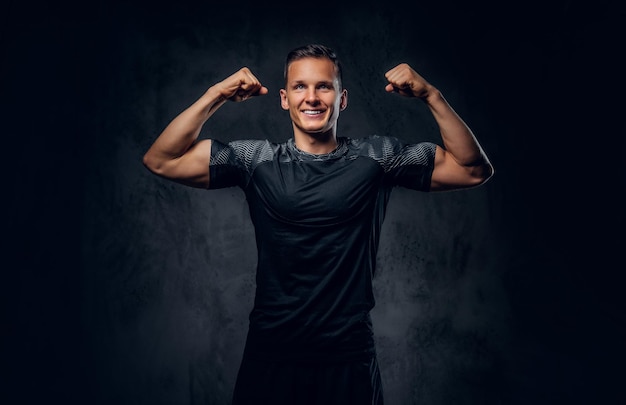 Athletic male dressed in a dark sportswear shows his biceps on grey background.