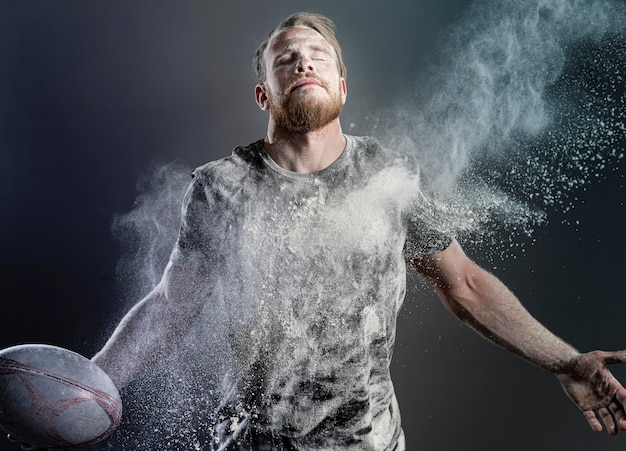 Foto gratuita giocatore di rugby maschile atletico che tiene palla con polvere