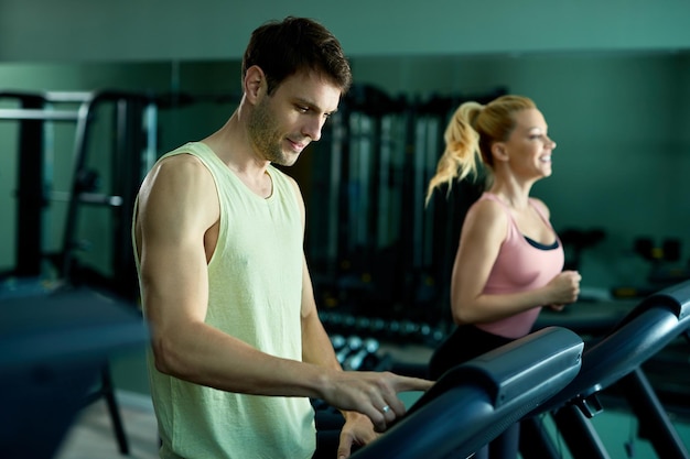 Athletic man adjusting speed while running on a treadmill in health club