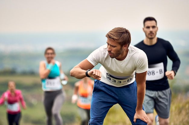 Foto gratuita uomo atletico che controlla la sua frequenza cardiaca sull'orologio intelligente dopo aver corso la maratona in natura