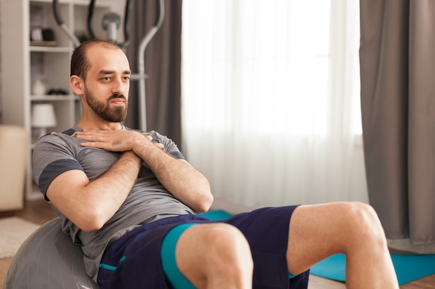 Athletic man doing abs workout on swiss ball in home during coronavirus lockdown.