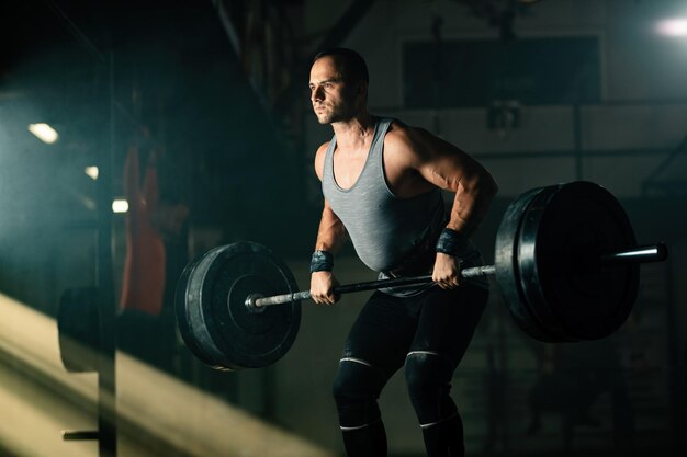 Athletic man exercising with barbell during cross training in health club