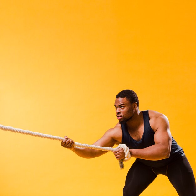 Athletic man in gym outfit pulling rope with copy space