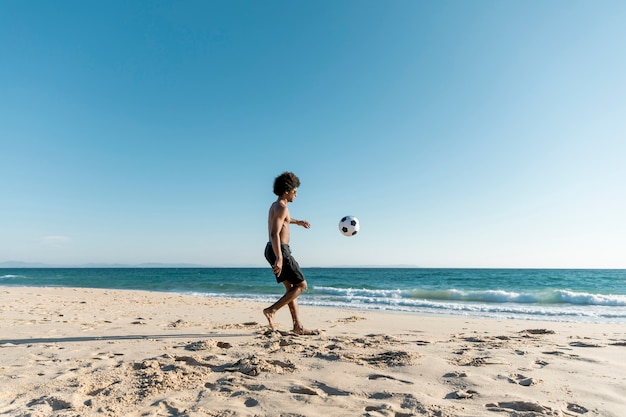 Athletic man kicking ball on beach