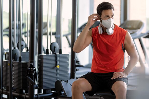 Athletic man preparing for workout and putting on protective face mask in a gym