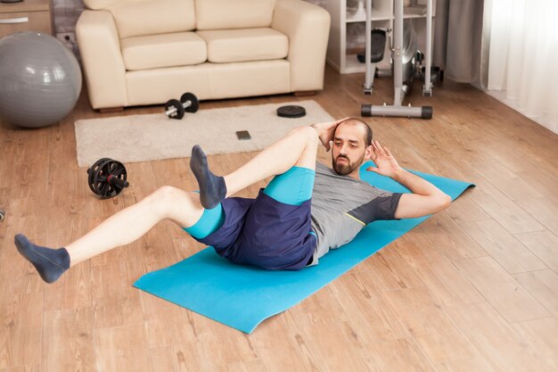 Спортивный мужчина тренирует живот на коврике для йоги во время глобальной пандемии.