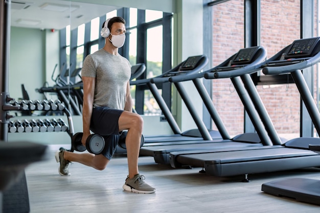 Athletic man with face mask having weight training in lunge position in a gym