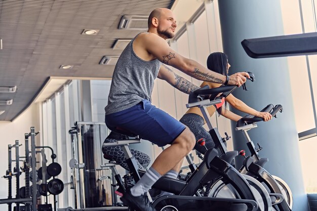 Athletic shaved head male and two slim fitness female exercising with body bike in a gym club.