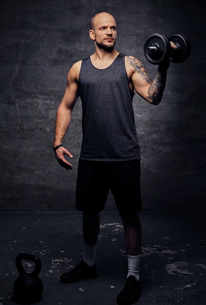 Athletic shaved head tattooed male doing shoulder workout with dumbbell.