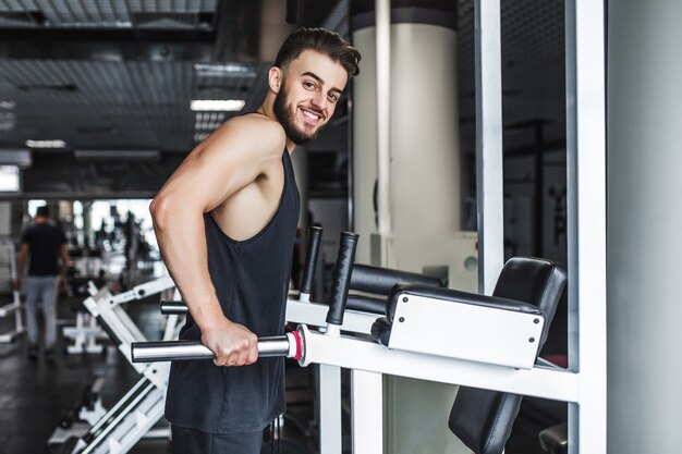 Athletic shirtless male doing workouts on a back with power exercise machine in a gym