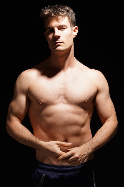 Athletic shirtless male standing confidently over black background
