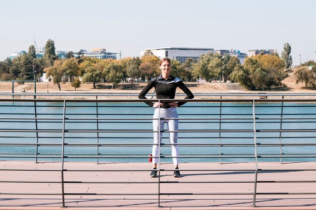 Athletic sportswoman standing behind the railing near the lake