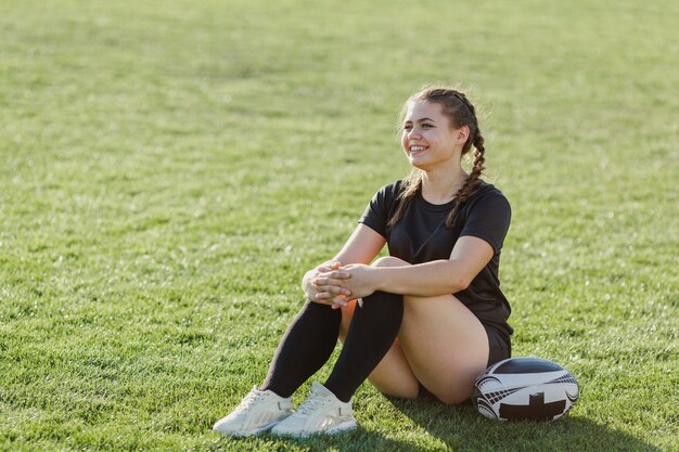 ラグビーボールの横にある草の上に座って運動の女性