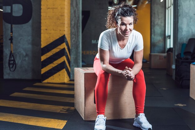 An athletic woman sitting on wooden box in fitness club