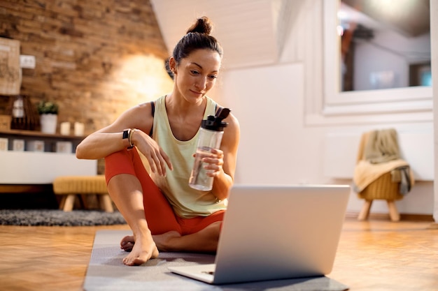 Athletic woman using laptop while having water break at home