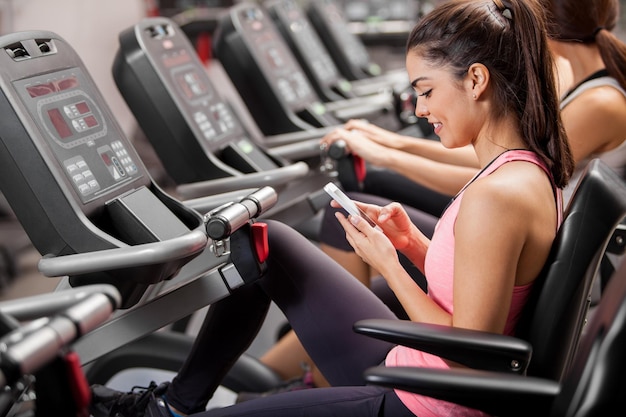 Foto gratuita atletico giovane bruna social networking e sms durante una lezione di spinning in palestra