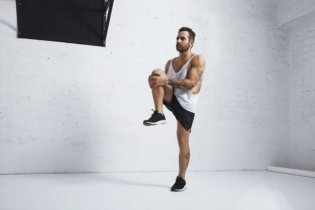 Athletic young man doing knee raises, stretching his legs