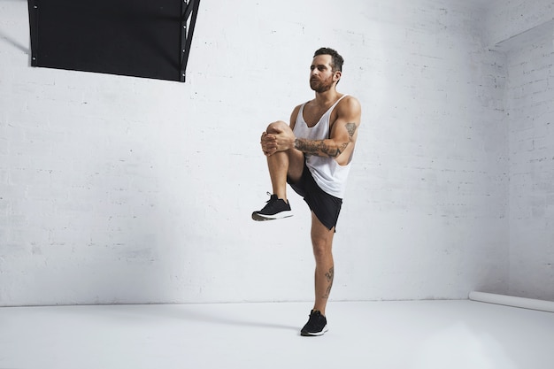 Athletic young man doing knee raises, stretching his legs