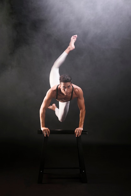 Free photo athletic young man jumping and leaning on wooden stand while looking at camera