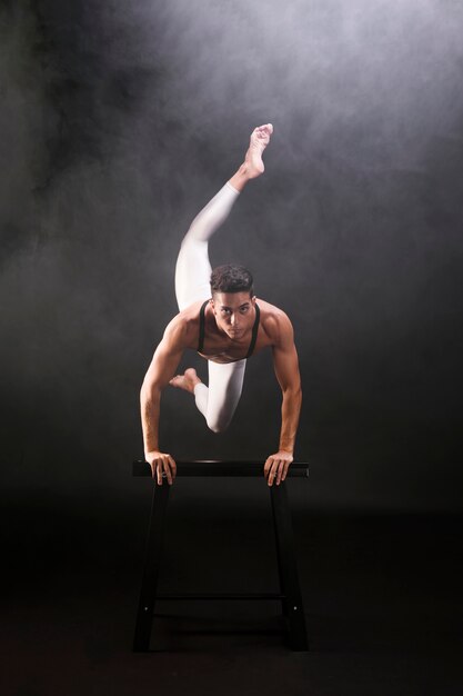 Athletic young man jumping and leaning on wooden stand while looking at camera