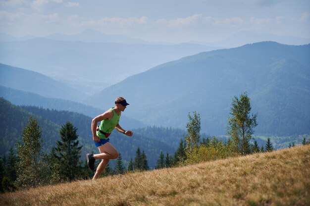 Athletic young man running up the hill in mountains