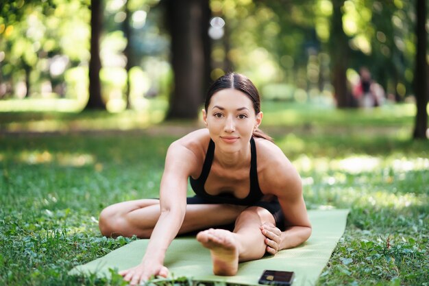 Спортивная (ый) молодая женщина занимается йогой в парке утром, женские тренировки на коврике для йоги