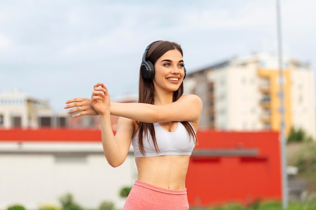 Athletic young woman with towel smiling and streaching Young sporty woman training Woman Doing Workout Exercises On Street Fit girl streaching before active fitness training