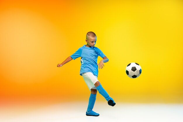 Attack. Young boy as a soccer or football player in sportwear practicing on gradient yellow in neon light