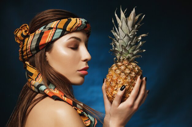 Attarctive woman with headband on forehead holding pineapple in hands.