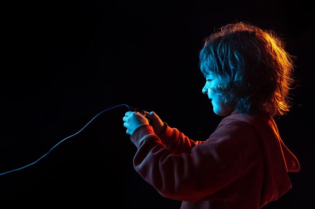 Attented playing videogames. Caucasian boy's portrait on dark studio background in neon light. Beautiful curly model.